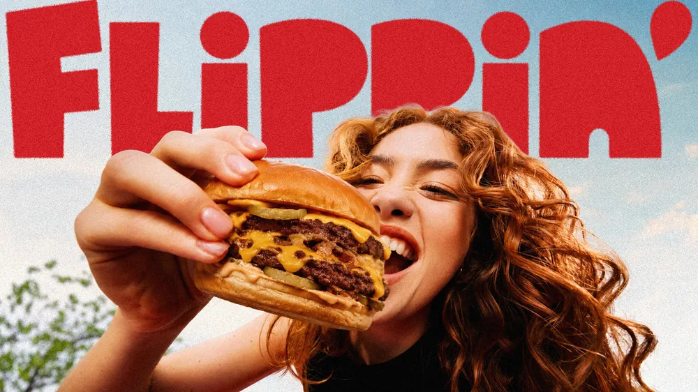 Smash burger Flippin' addentato, con il logo FLiPPiN' sullo sfondo